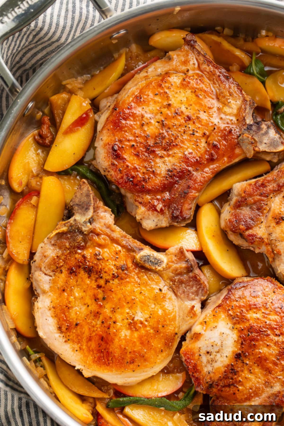 Seared pork chops with apples and a sage butter sauce in a large silver skillet.