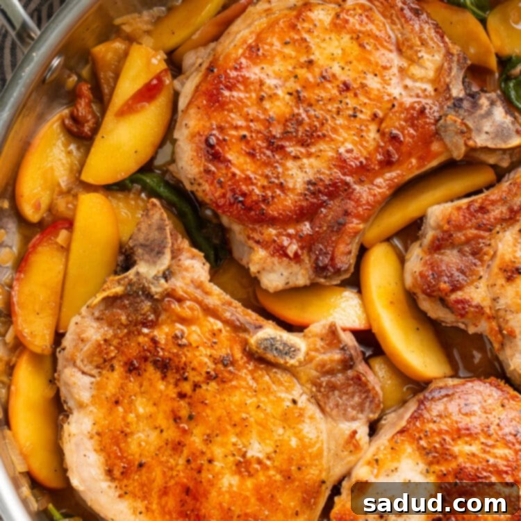 Seared pork chops with apples and a sage butter sauce in a large silver skillet.