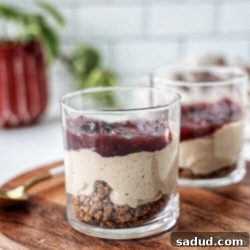 A vibrant single-serve vegan protein cheesecake jar with a crumbly base and a berry jam topping.