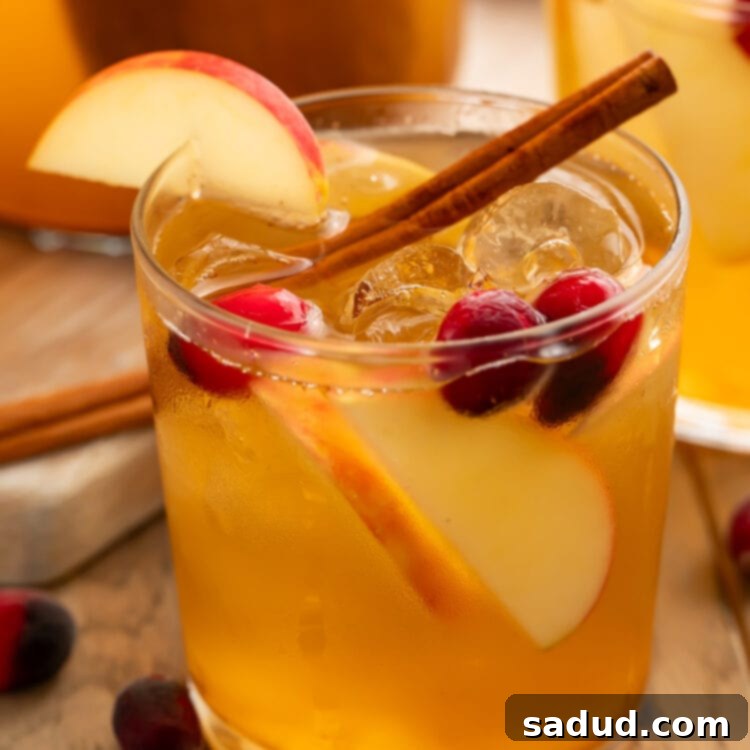 An apple cider sangria in a glass garnished with apples, grapes, and a cinnamon stick.