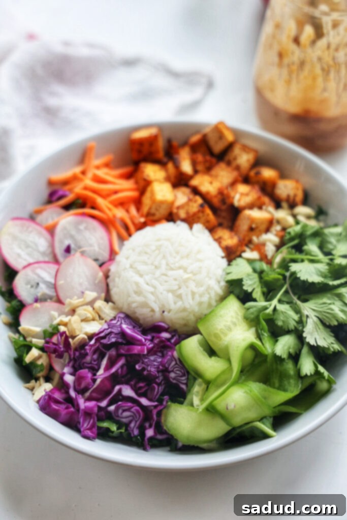 A vibrant and colorful Thai nourish bowl filled with a mix of fresh vegetables, crispy tofu, and rice, drizzled with creamy peanut sauce.