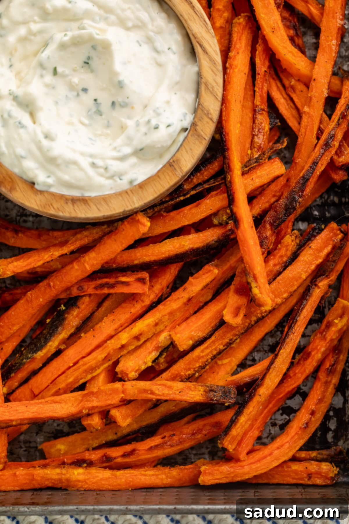 Crispy Carrot Fries 3 Close up of a tray of baked carrot fries with a creamy bowl of dip in the top left hand corner.