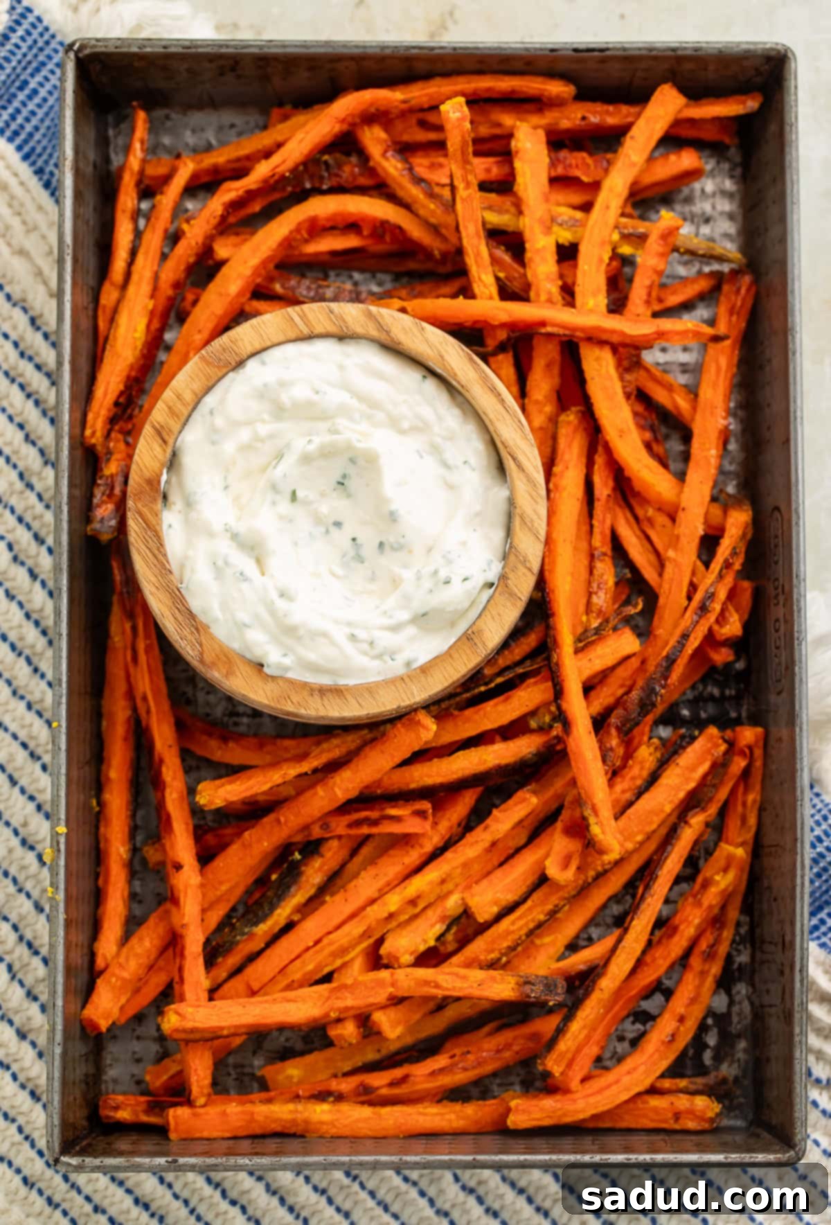 Crispy Carrot Fries 4 Top down view of a baking tray of carrot fries with a wooden bowl of creamy dip placed in the middle.