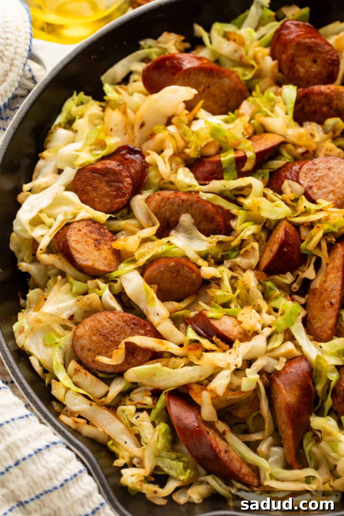 Close-up of golden-brown kielbasa and tender, wilted cabbage in a large skillet.