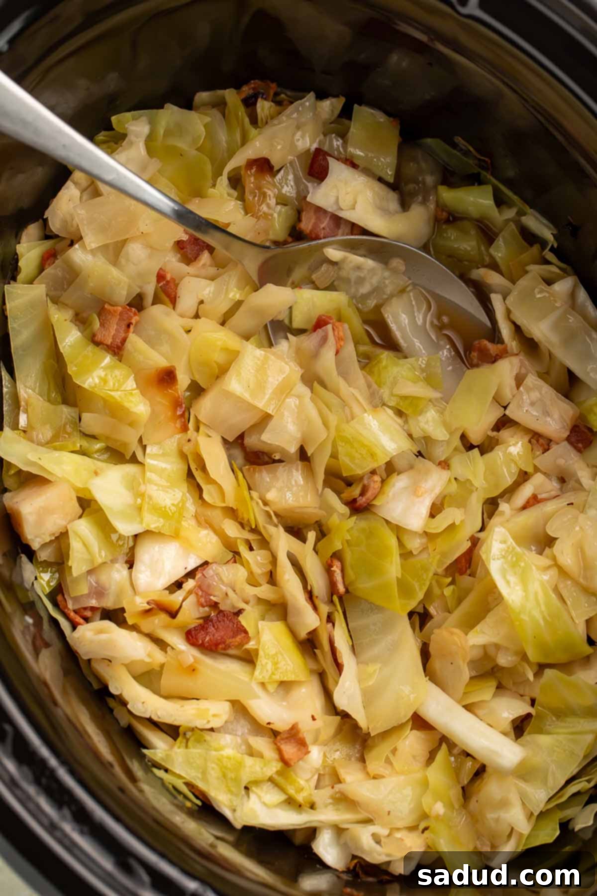 Tender Slow Cooker Cabbage 2 Crockpot cabbage in a slow cooker with a large silver spoon, highlighting the rich, savory textures ready to be served.