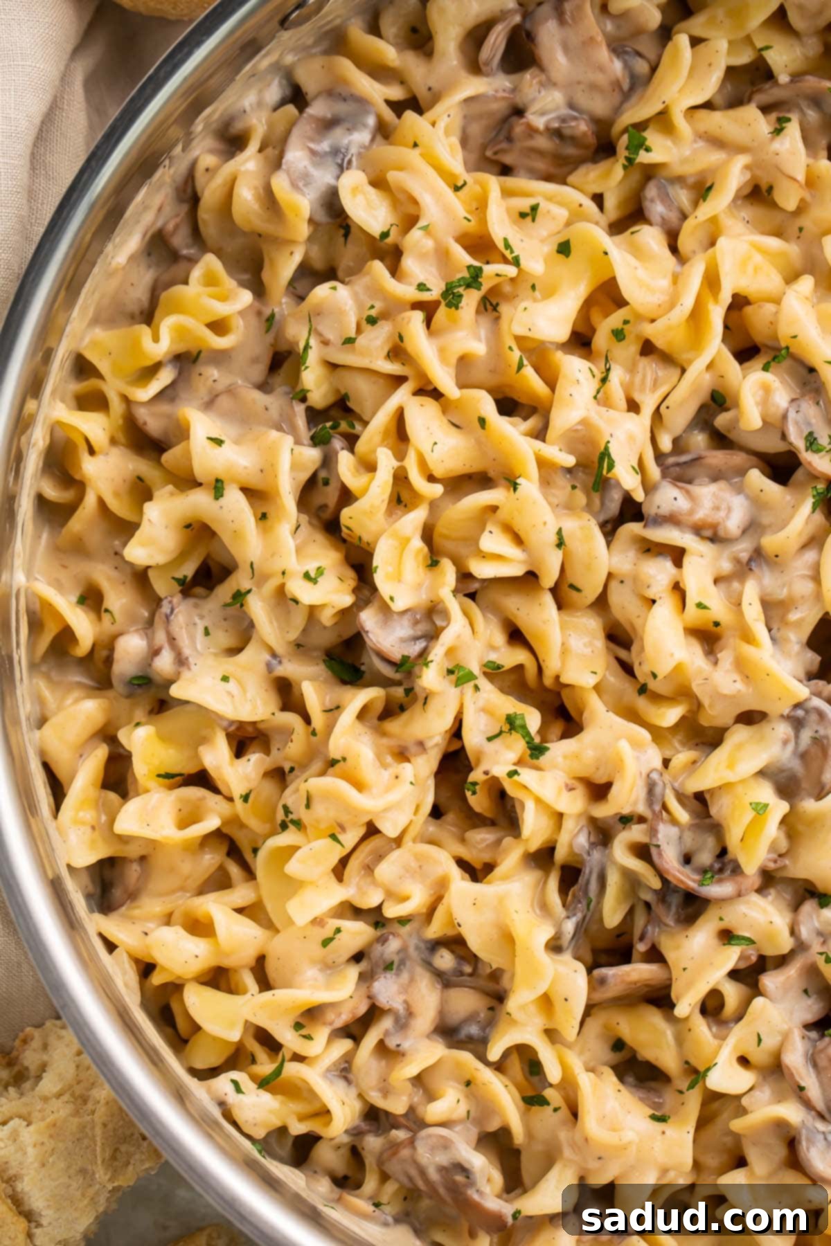 A large stainless skillet holding creamy mushroom stroganoff made with wide egg noodles and pieces of baby bella mushrooms, ready to be served.