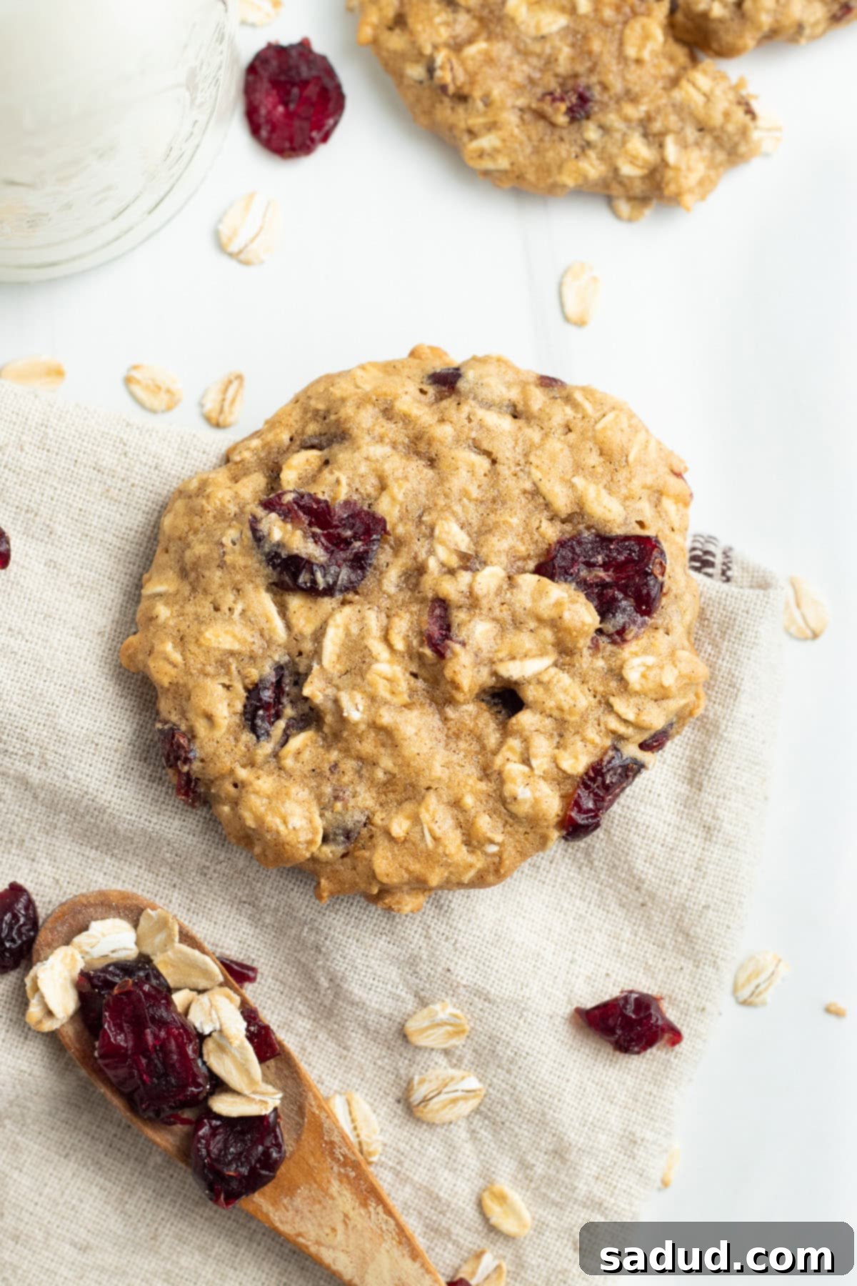 Overhead view of cranberry oatmeal cookie on a napkin next to a wooden spoon with cranberries and oats.