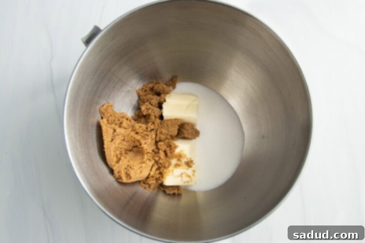 Overhead view of butter, brown sugar, and white sugar in a large metal mixing bowl from a stand mixer.