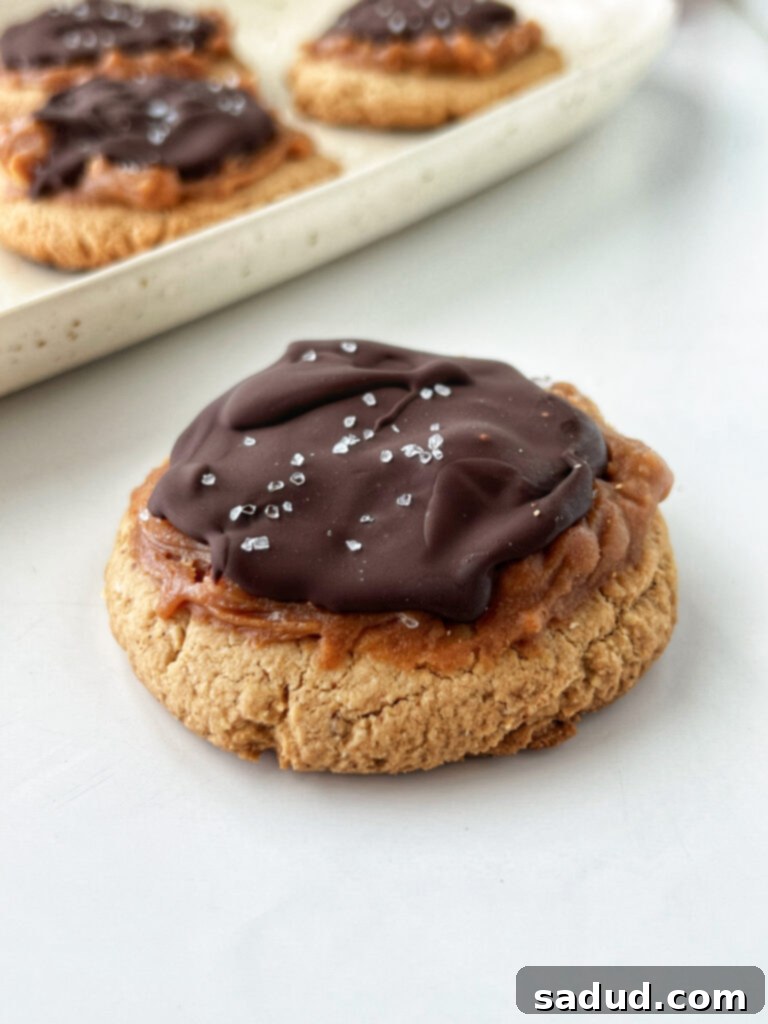 Close-up of a single vegan Twix cookie, showing the rich chocolate topping and the gooey caramel layer beneath.