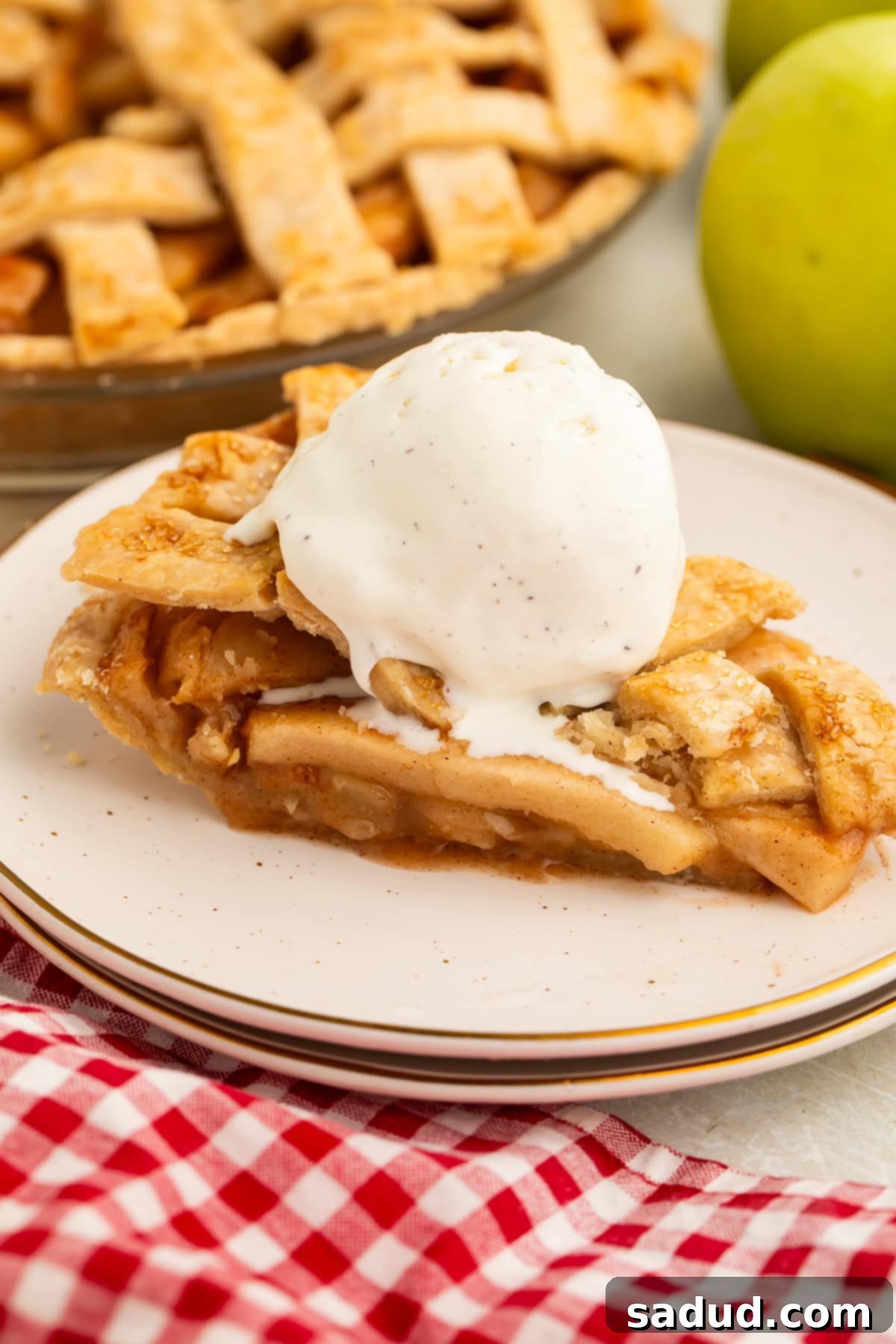 A slice of warm, crisp vegan apple pie topped with a scoop of vanilla bean vegan ice cream rests on a plate.