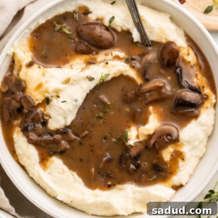 Irresistible Vegan Mushroom Gravy 4 A large bowl of mashed potatoes generously topped with rich brown vegan mushroom gravy, ready to be served.
