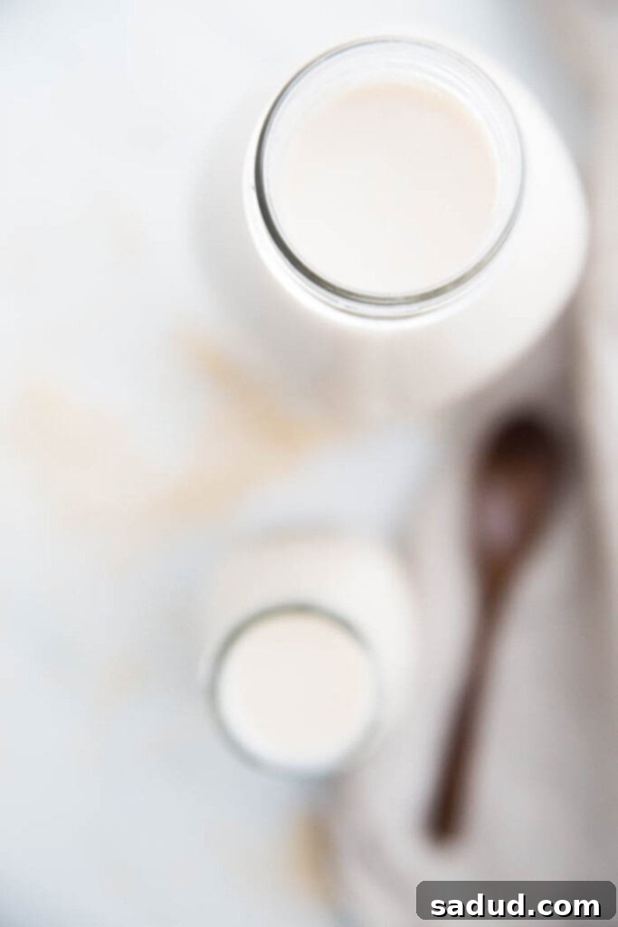overhead image of homemade oat milk in glass container with oats scattered around
