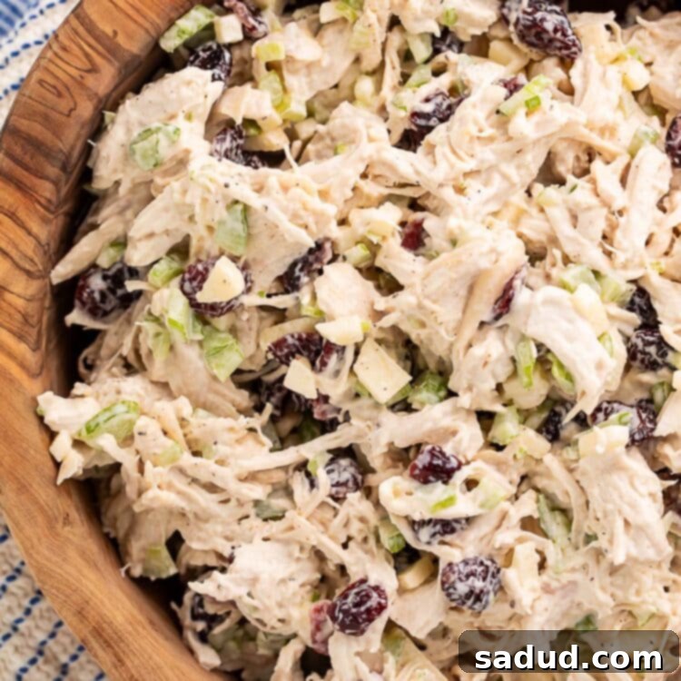 A large wooden bowl of cranberry chicken salad next to a blue and white kitchen towel.