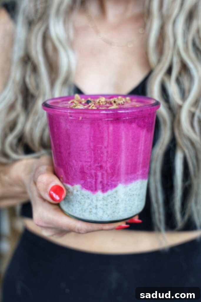 Vibrant layered dragonfruit chia smoothie jar with a spoon, showing the distinct pink smoothie layer over the lighter chia pudding layer, topped with granola.