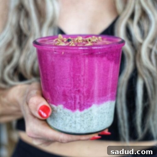 chia pudding dragonfruit smoothie breakfast jar bowl. A close-up of a vibrant layered smoothie with pink dragonfruit smoothie on top and white chia pudding below, garnished with granola and fresh fruit.