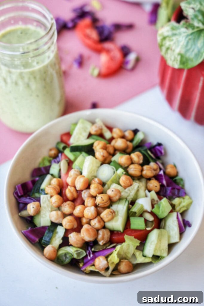 Vibrant homemade vegan tahini basil salad dressing drizzled over a fresh salad of lettuce, chickpeas, chopped tomatoes, and red cabbage, highlighting its rich texture and color.