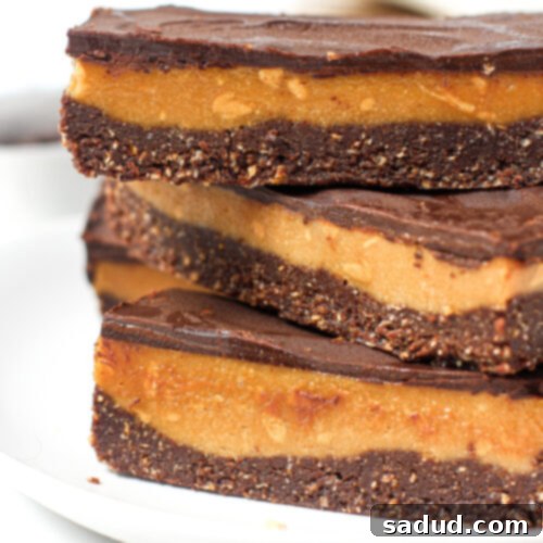A stack of healthy no-bake peanut butter bars, showcasing their chocolate base, creamy peanut butter caramel, and rich chocolate topping.
