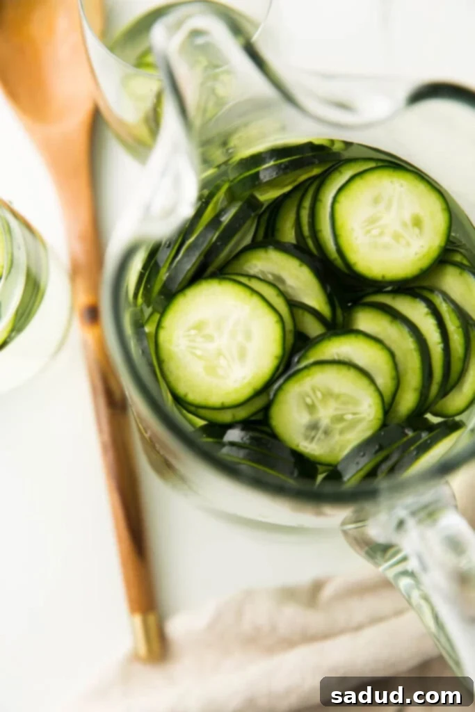 Beat the Heat: Homemade Cucumber Water 4 Overhead shot of thinly sliced cucumbers submerged in water within a clear glass pitcher, ready for infusion.