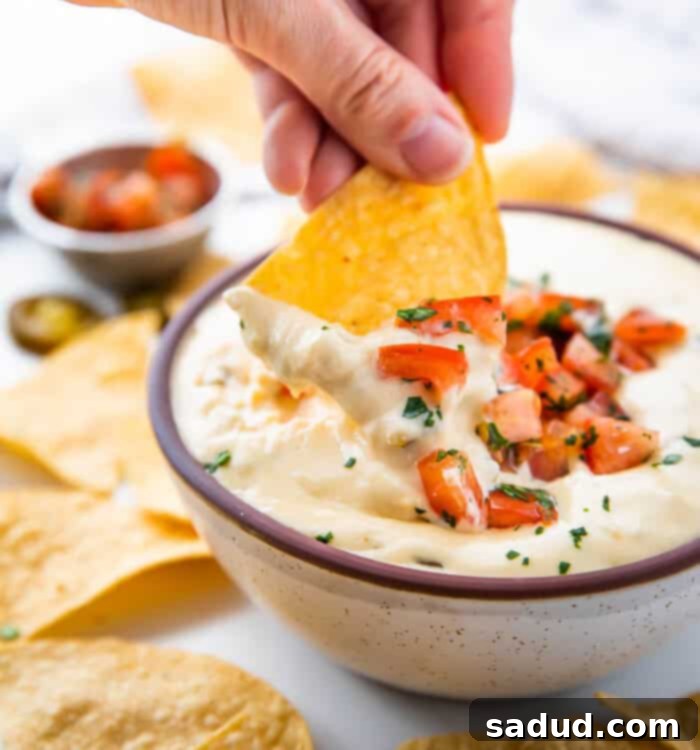 Effortless Slow Cooker Queso 6 A chip being dipped into a bowl of the perfectly creamy and delicious Crockpot Queso Dip.