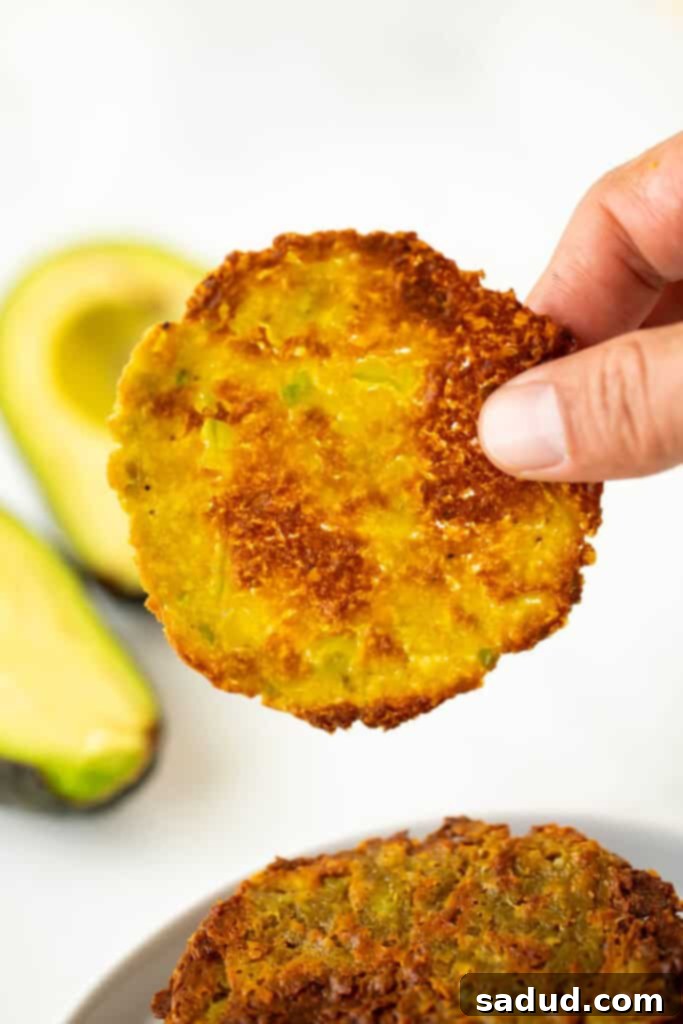 A hand holding a single perfectly golden and crispy avocado chip, showcasing its texture and deliciousness.