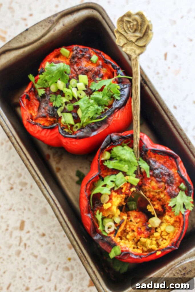 Two vibrant quinoa stuffed bell peppers in a baking dish, drizzled with peanut sauce and garnished with fresh herbs, ready to be served.
