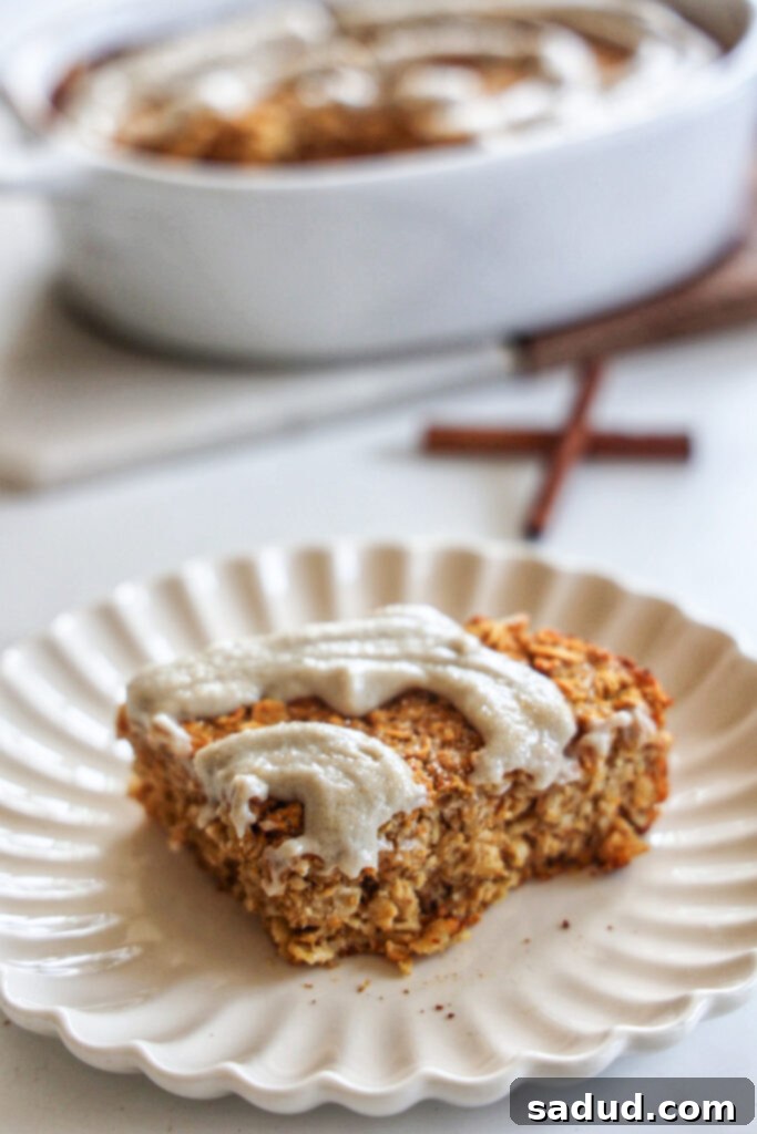 Cozy Pumpkin Baked Oatmeal 4 A slice of Baked pumpkin oatmeal with cashew cream frosting on a white plate, garnished with cinnamon.
