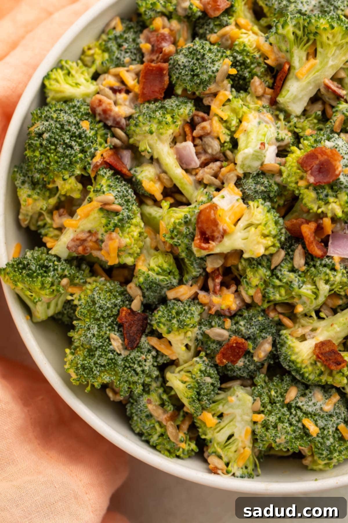 A close-up of the top of a large white bowl filled with a keto salad made with chopped broccoli florets, bacon, cheddar cheese, red onion, and a light mayo dressing.