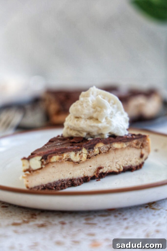 A slice of vegan snickers cheesecake on a white plate with whipped cream, showing off its beautiful layers.