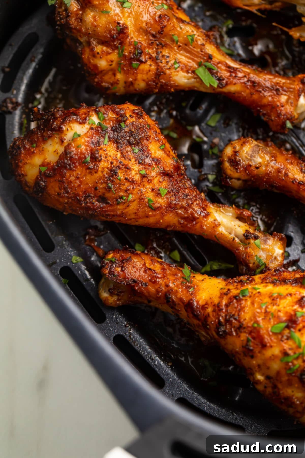 Close up of air fryer chicken legs in a black air fryer basket, showcasing crispy skin.