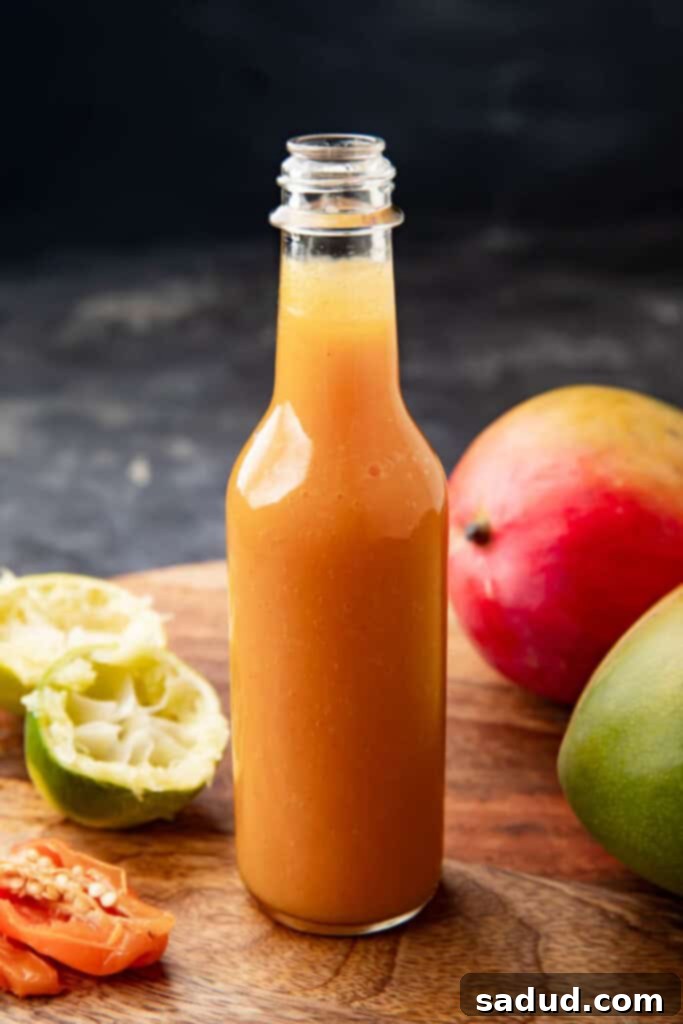 Jar of homemade mango habanero sauce with fresh mango and habanero peppers in the background, perfect for adding sweet and spicy flavor to wings and other dishes.