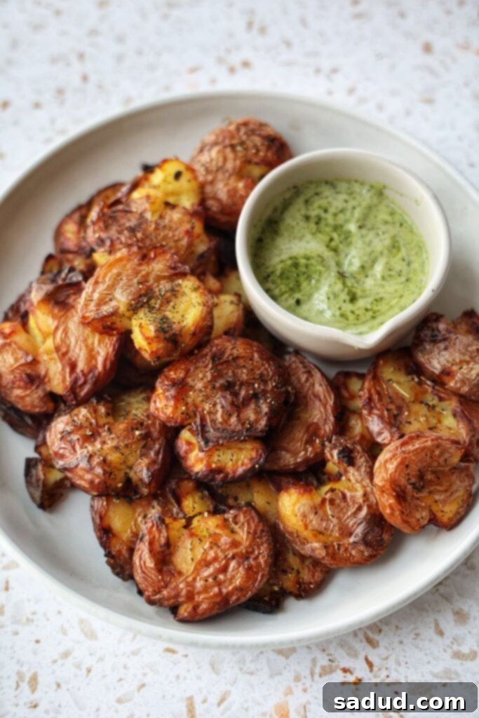A plate of crispy garlic smashed potatoes with a side of pesto aioli for dipping.