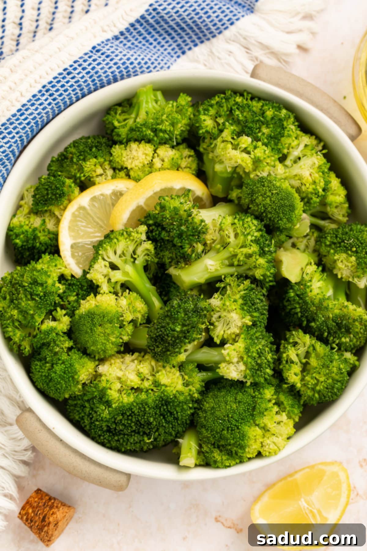 Bowl of cooked broccoli garnished with lemon slices in a white bowl.