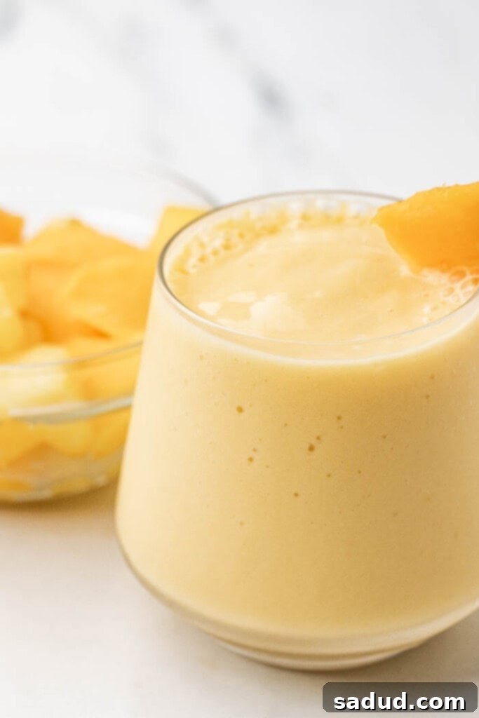 A refreshing glass of creamy mango pineapple smoothie, garnished with fresh fruit, ready to be enjoyed.