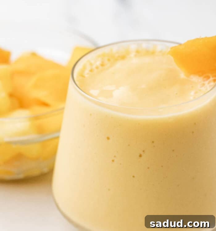 Close-up of a glass of vibrant mango pineapple smoothie, topped with a straw, showing its thick and creamy texture.