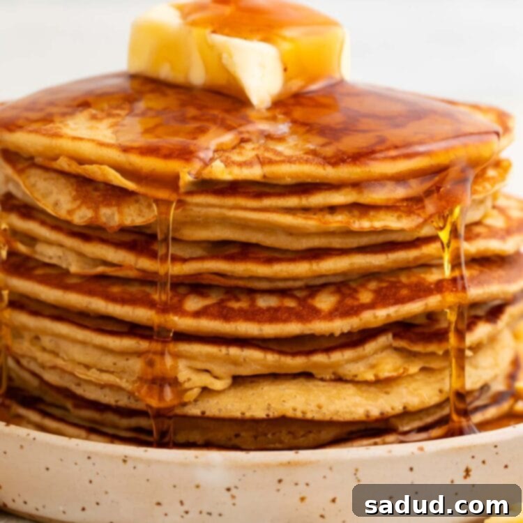 A beautifully presented stack of fluffy peanut butter pancakes, crowned with a dollop of butter and a cascading syrup drizzle, tempting for breakfast or brunch.