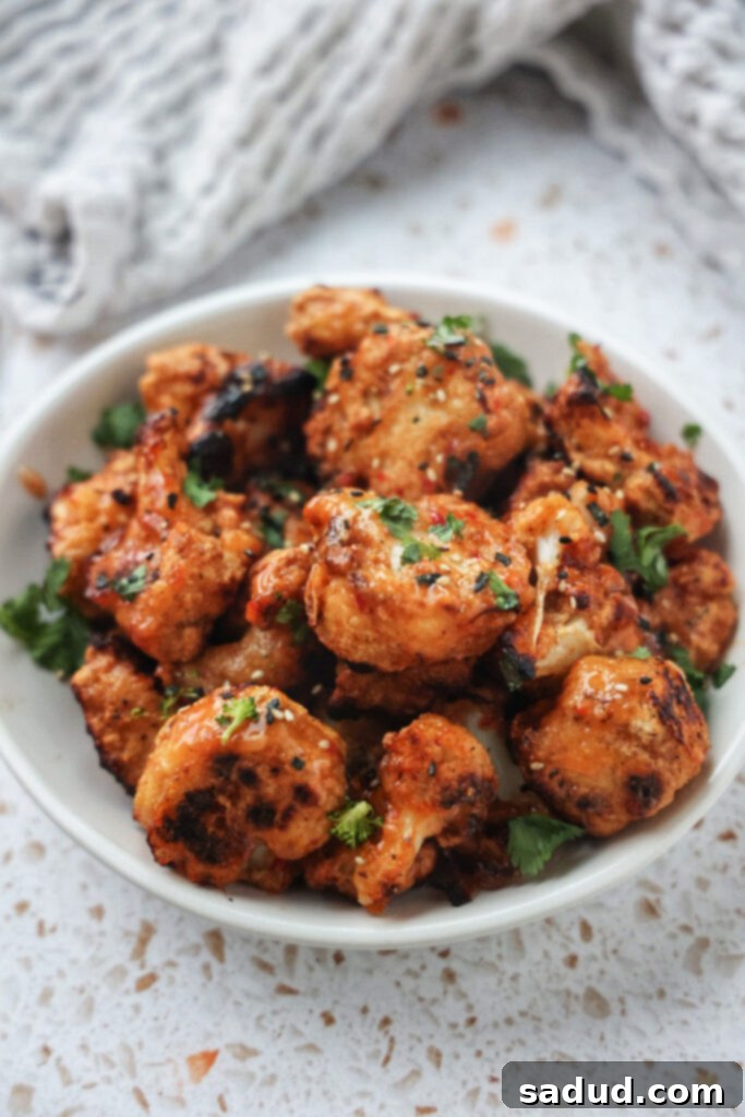 A bowl of sweet and spicy cauliflower wings garnished with green onions and sesame seeds.
