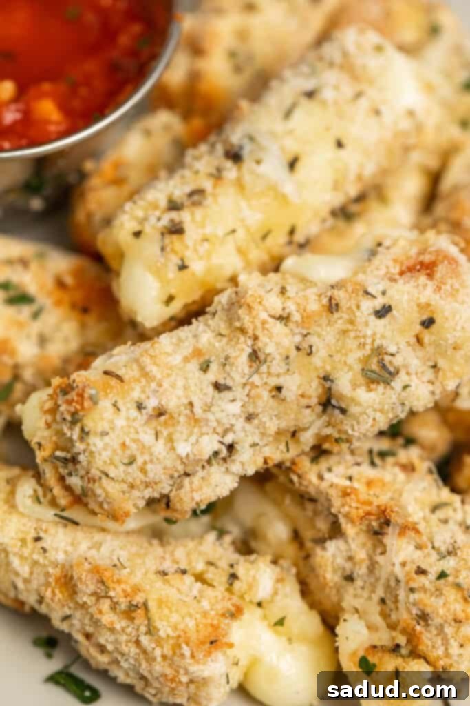 Close-up view of homemade air fryer mozzarella sticks seasoned with Italian spices piled up next to a bowl of marinara sauce. The sticks are golden and crispy, with melted cheese peeking out, inviting a bite.