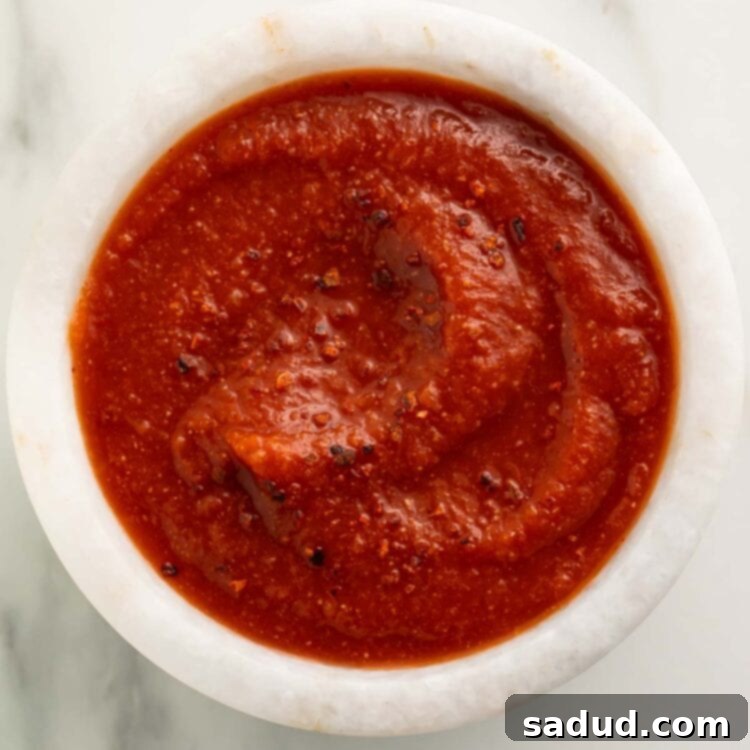 Top-down view of a small white bowl of deep red taco sauce on a marble countertop.