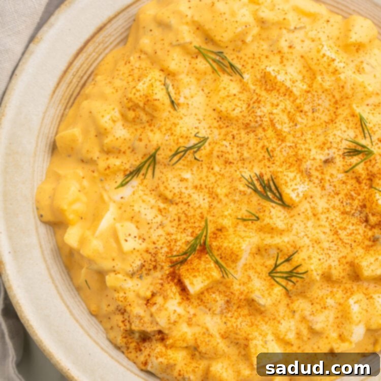 Close-up view of creamy deviled egg salad in a bowl on a neutral tabletop, garnished with paprika and fresh parsley.