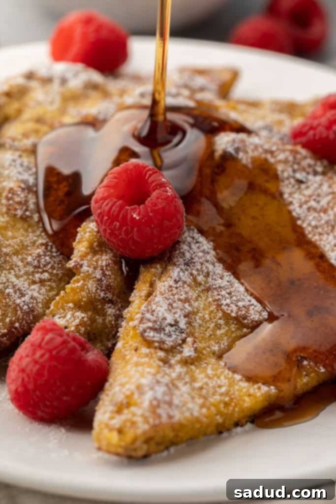 Sugar-free syrup generously pouring over golden-brown keto French toast, topped with a dusting of powdered erythritol and fresh raspberries for a vibrant and delicious low-carb breakfast.
