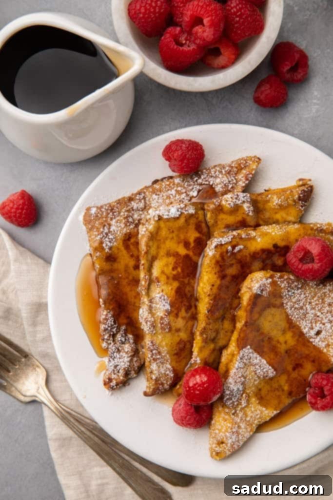 Three slices of golden-brown keto French toast stacked, garnished with powdered erythritol and fresh raspberries, and ready to be served.