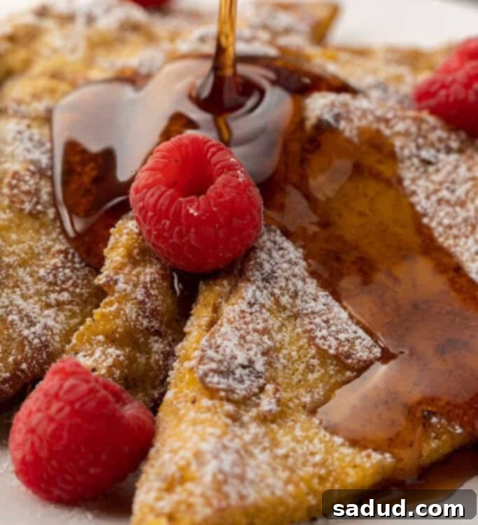 Sugar-free syrup drizzling over warm keto French toast, dusted with erythritol and adorned with fresh raspberries.