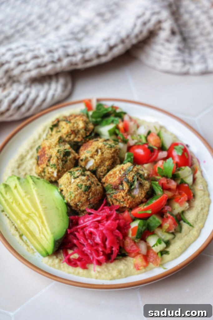 A vibrant hummus plate topped with crispy cauliflower falafel, fresh Shirazi salad, and creamy avocado.