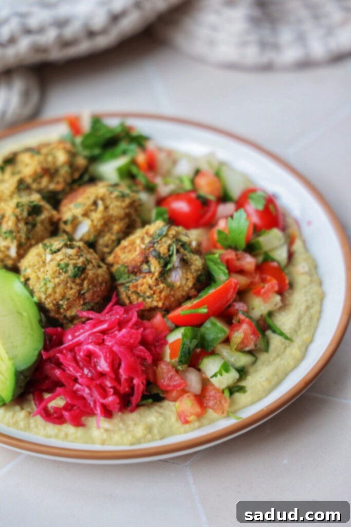 Close-up of baked cauliflower falafel on a hummus plate with fresh herbs and salad.