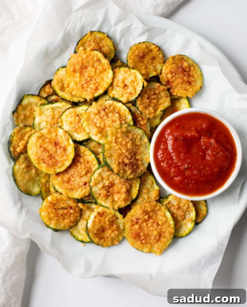 Air fryer zucchini chips cooling on a white plate after cooking, showing their crisp texture