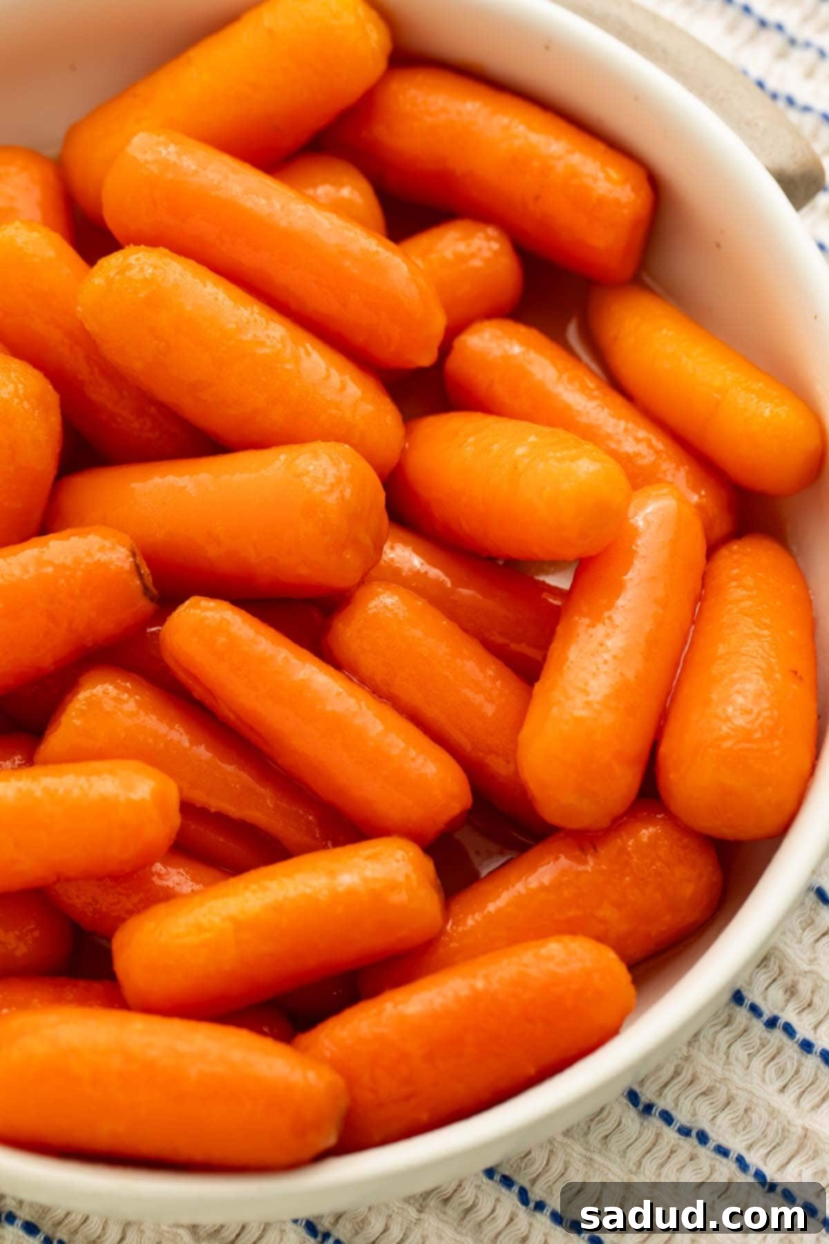 A white bowl holding buttery carrots cooked in the Instant Pot, drizzled with maple butter glaze and fresh parsley.
