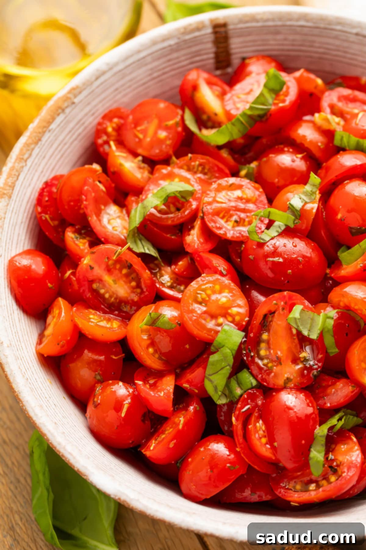 Top-down view of a bowl of rich, bright red tomatoes with fresh green basil in a white bowl. Perfect for a summer gathering.