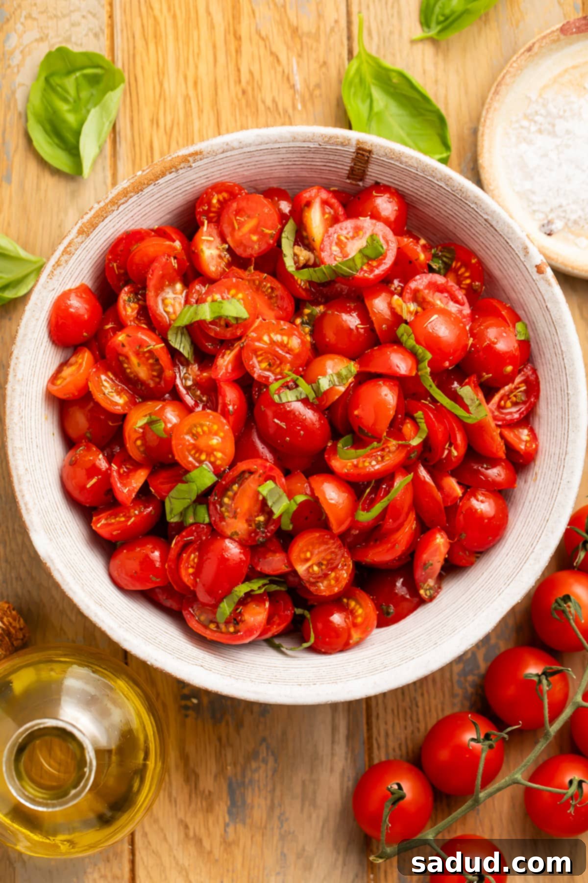 A large white bowl sits on a wooden table. In the bowl is a pile of sliced cherry tomatoes and strips of green fresh basil. Ready to serve.