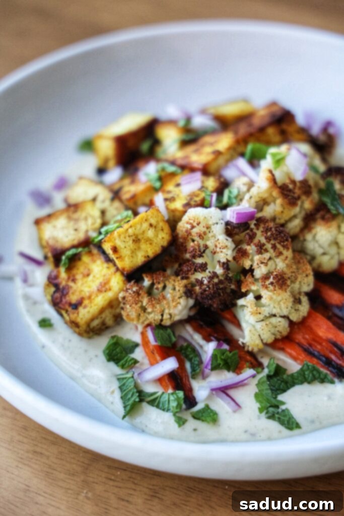 A close-up of a roasted veggie and tofu plate with a generous swirl of garlic tahini yogurt sauce.