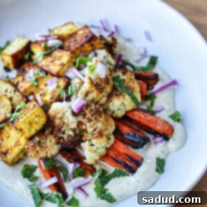 A plate of sheet pan roasted vegetables and tofu with a creamy garlic tahini yogurt sauce.
